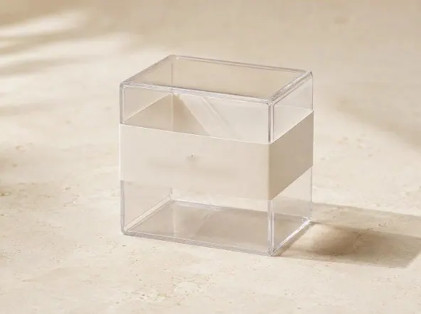 A clear acrylic gift box with a paper sleeve on a stone surface