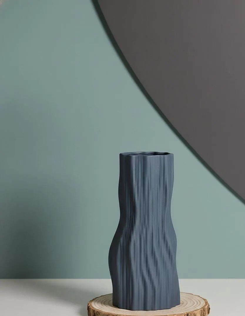 A navy ceramic vase with a rippled, wave-like form on a wood slice