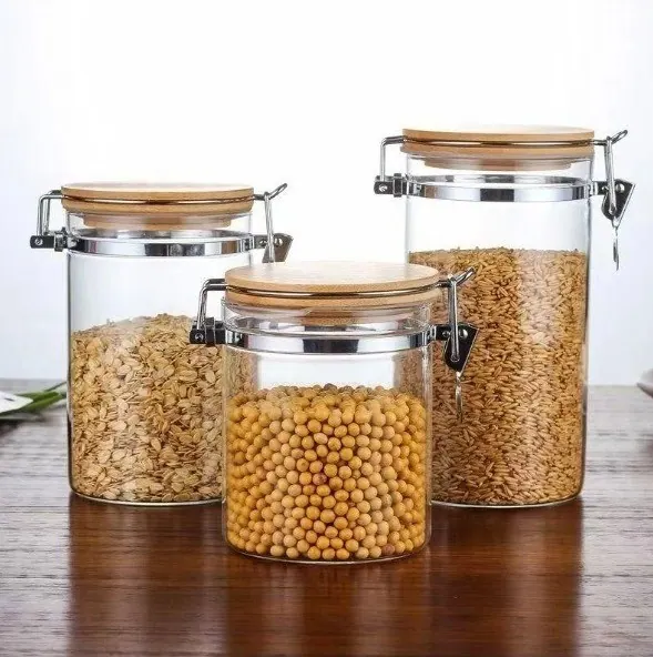 Three glass clamp-lid canisters with bamboo lids holding oats, chickpeas and rice