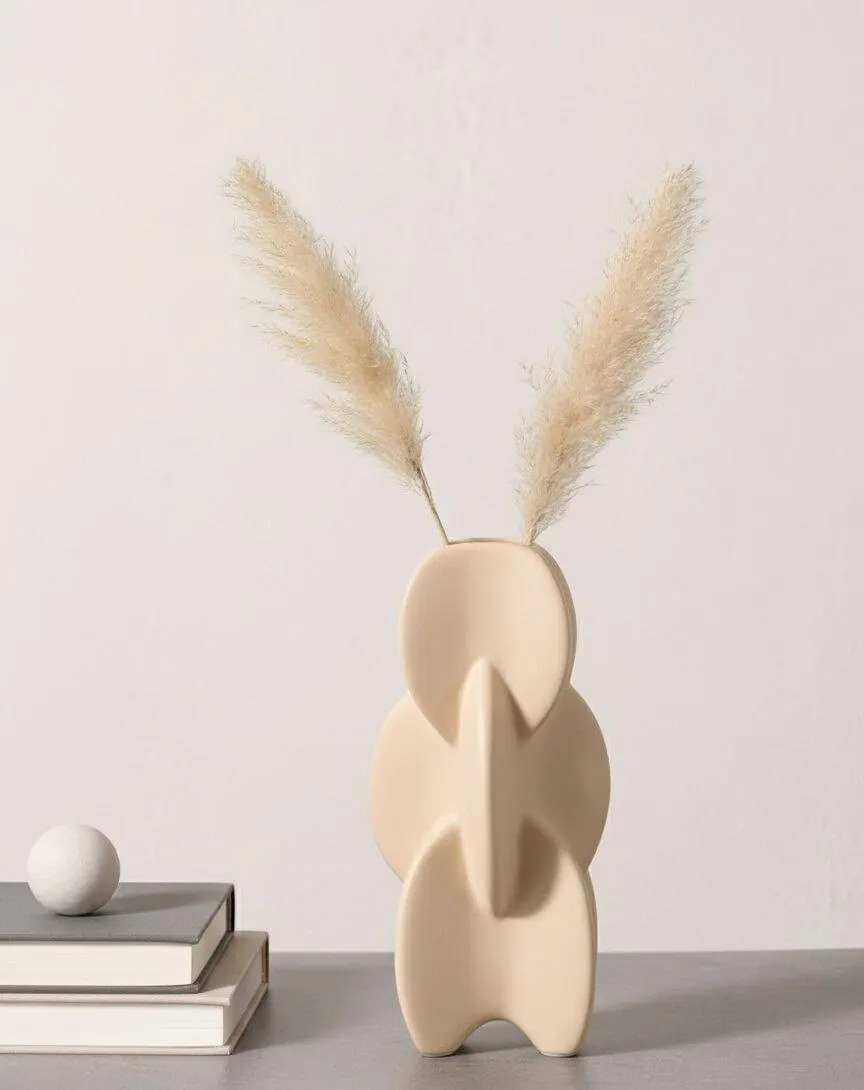 A cream sculptural vase with pampas stems beside stacked books