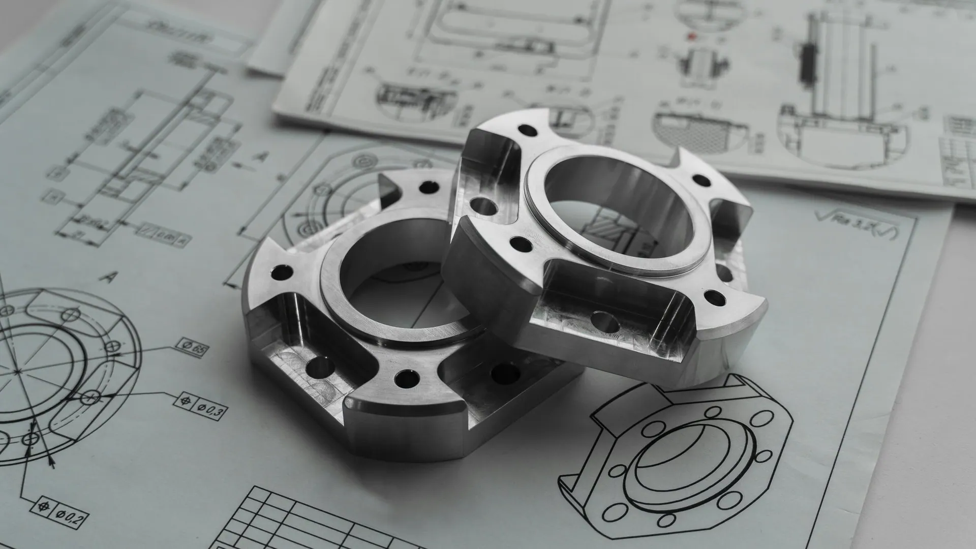 Machined metal components resting on engineering drawings