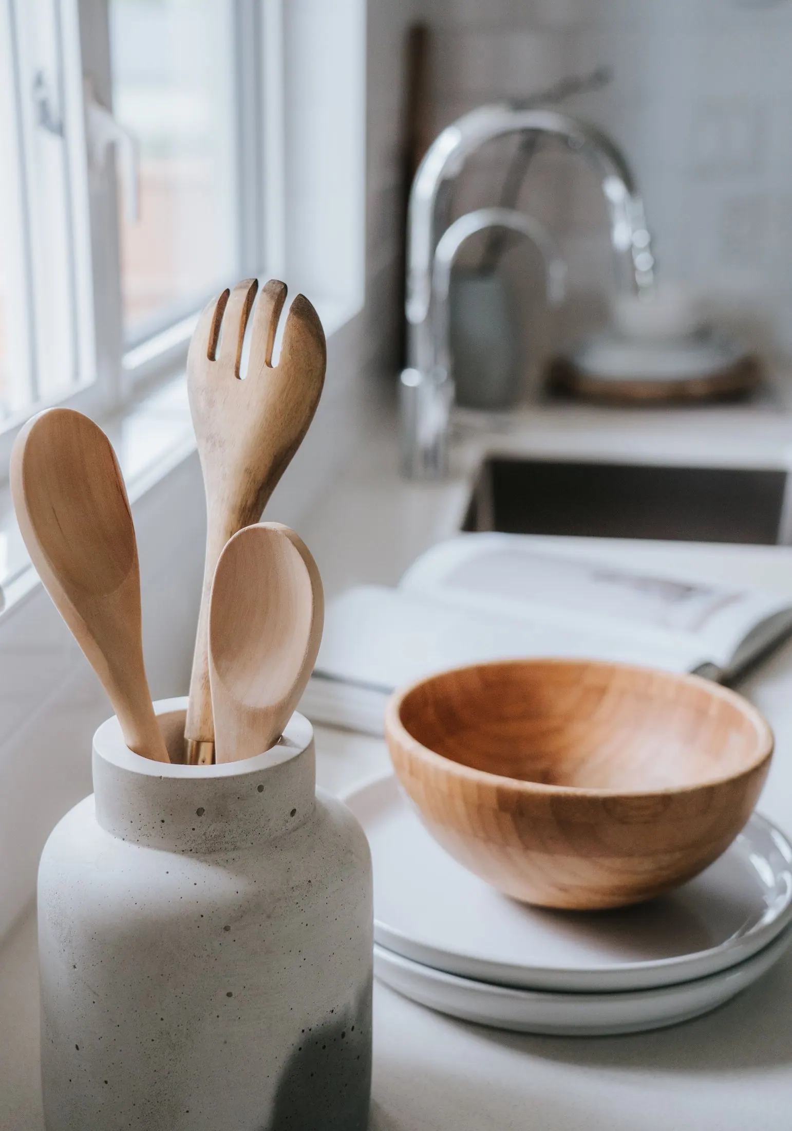 Wooden spoons in a stone crock beside a wooden bowl in a bright kitchen