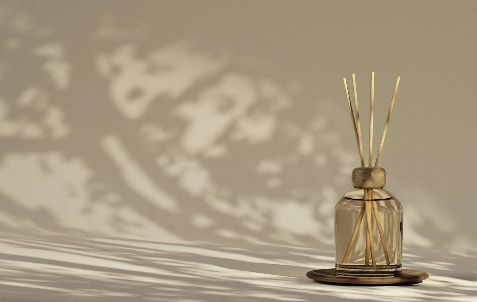 A smoked-glass reed diffuser on a tray with leaf shadows on a taupe wall