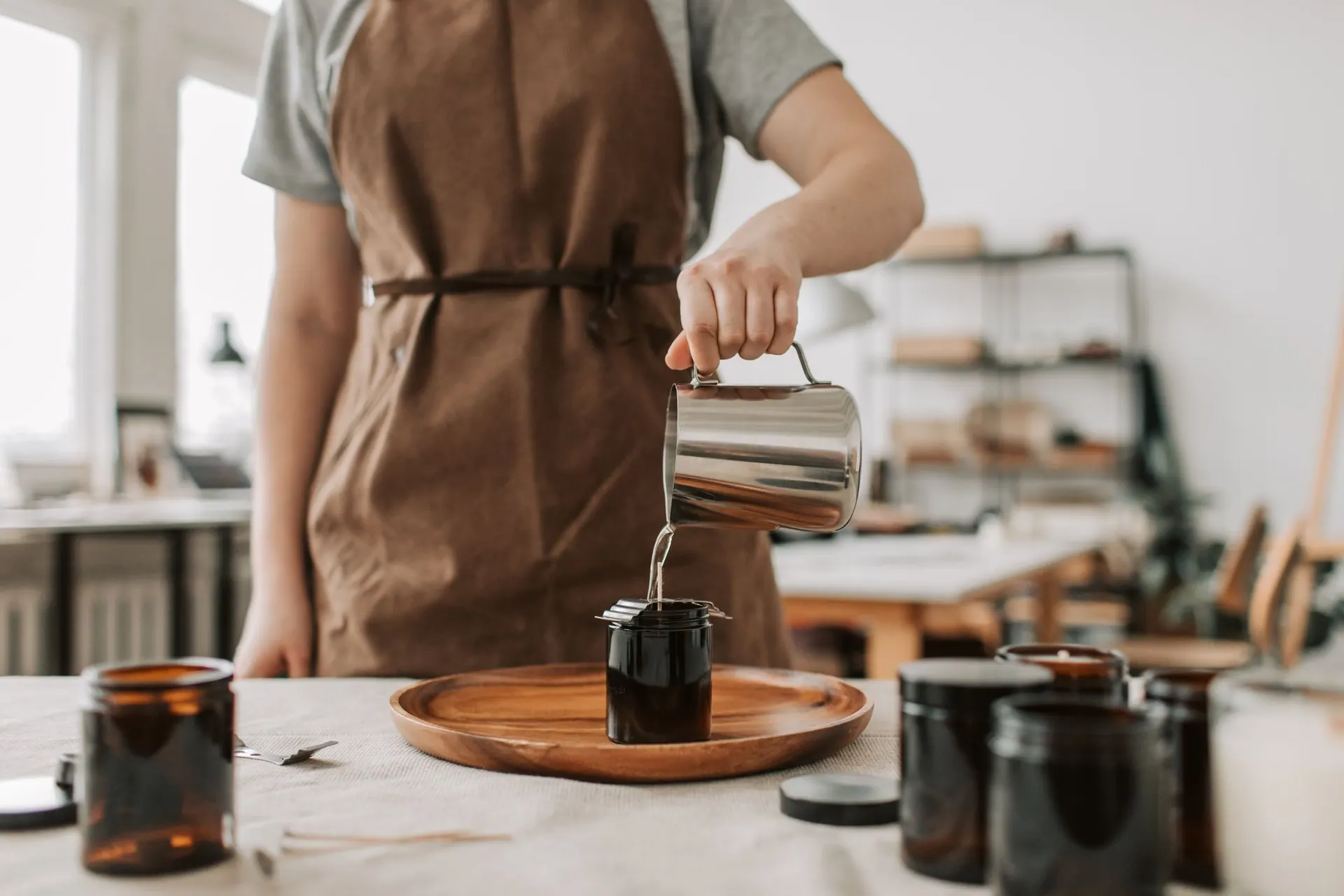 Hot wax being poured from a steel pitcher into amber jars